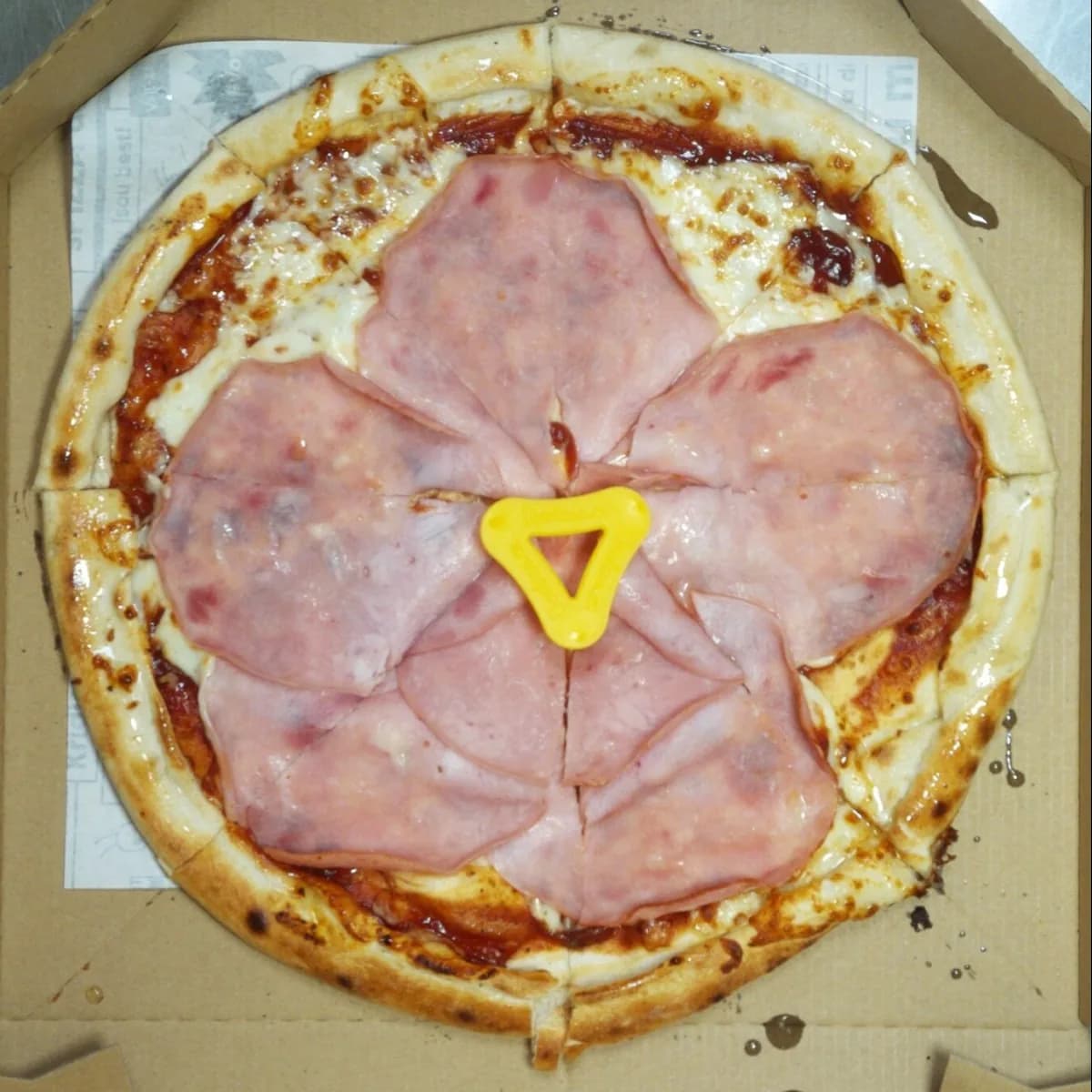 Camera photo of a ham pizza with a pale, underbaked crust, taken at the packing station