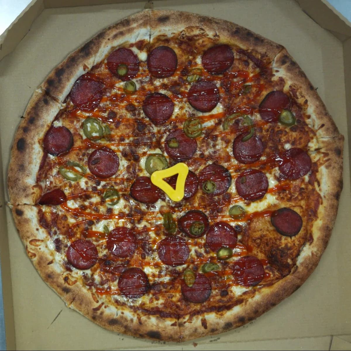 Pepperoni and jalapeño pizza with thin lines of sriracha