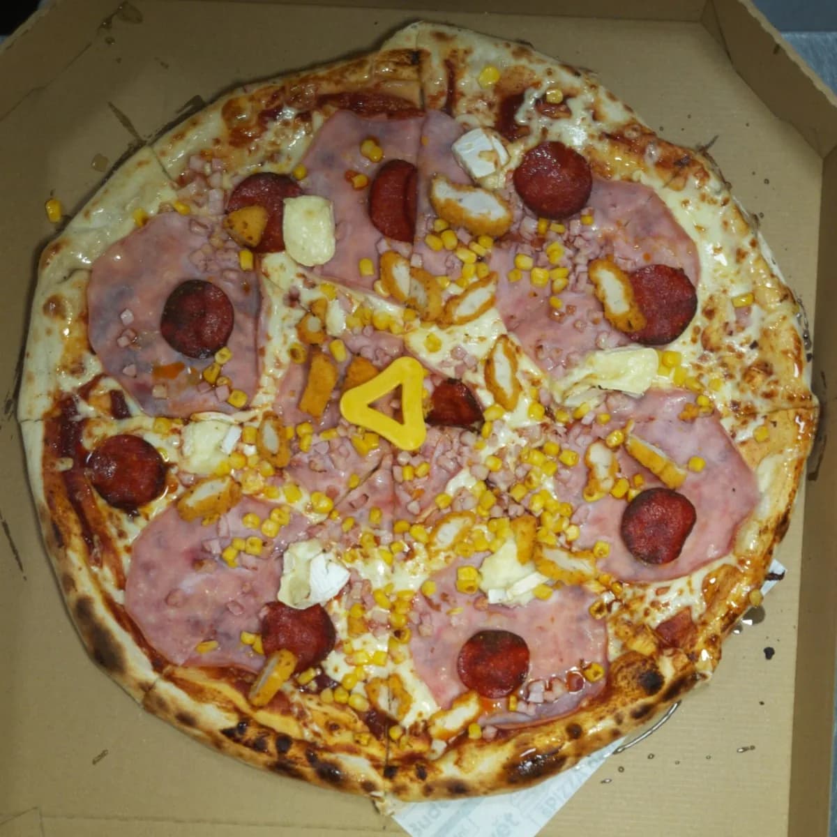 Pizza topped with ham, salami, camembert, chicken strips, bacon bits, and corn